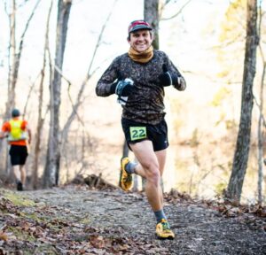 Matt Amonette smiles at camera while trail running in woods