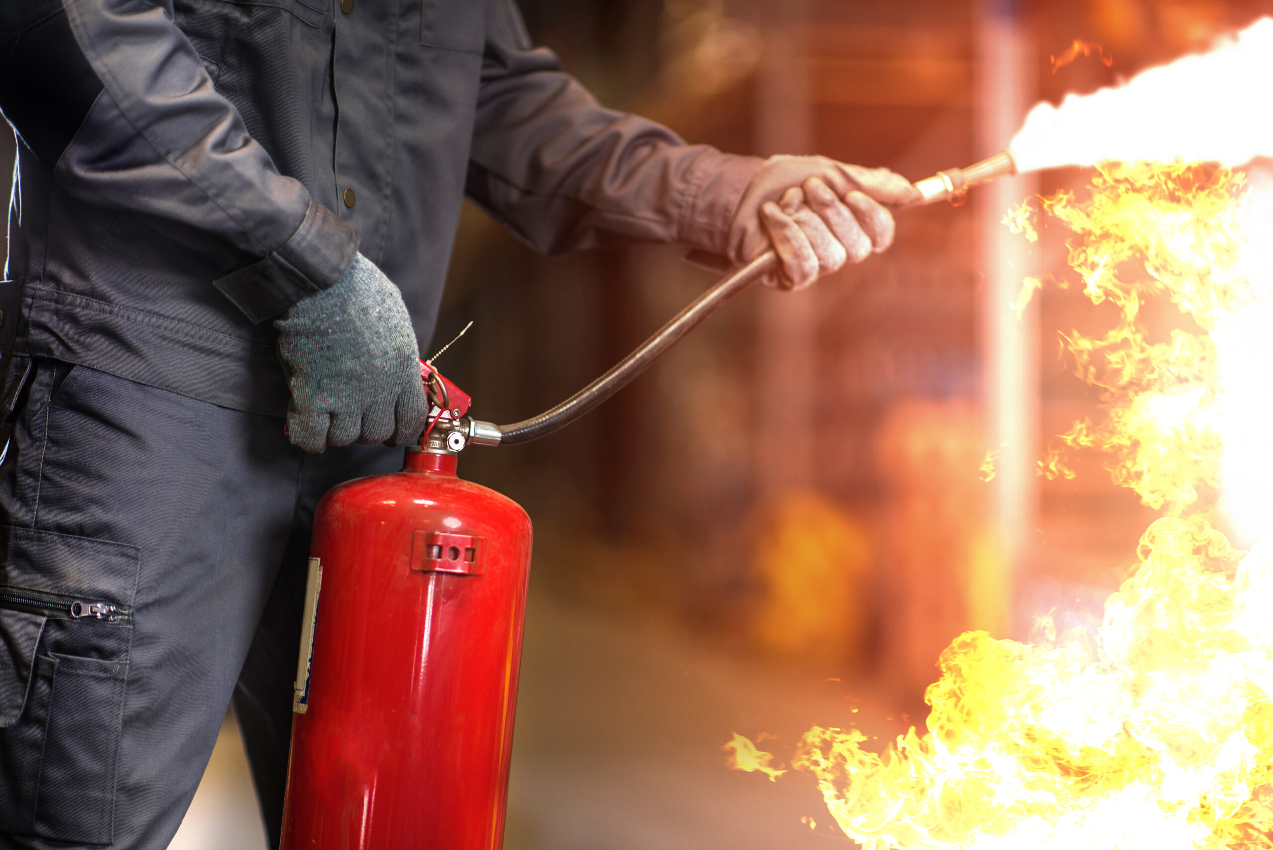 Photo: closeup of a person using a fire extinguisher with flames on the right side of the image.
