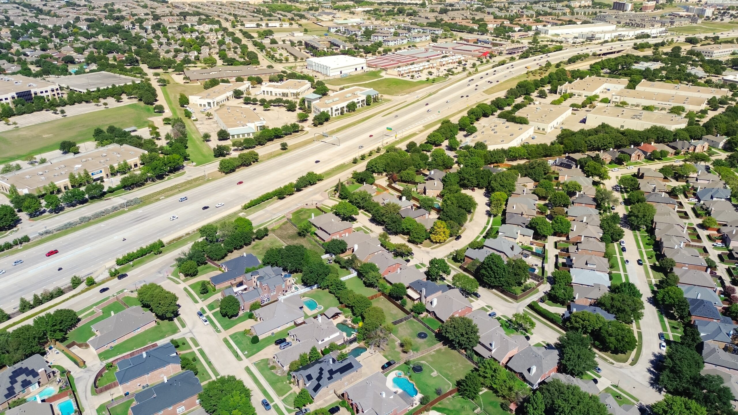Birds-eye view of a city bisected by a highway with residential homes below and commercial buildings above.