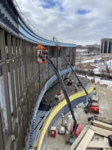 Side view of a curbed building accessed by workers in lifts for a building enclosure design project.