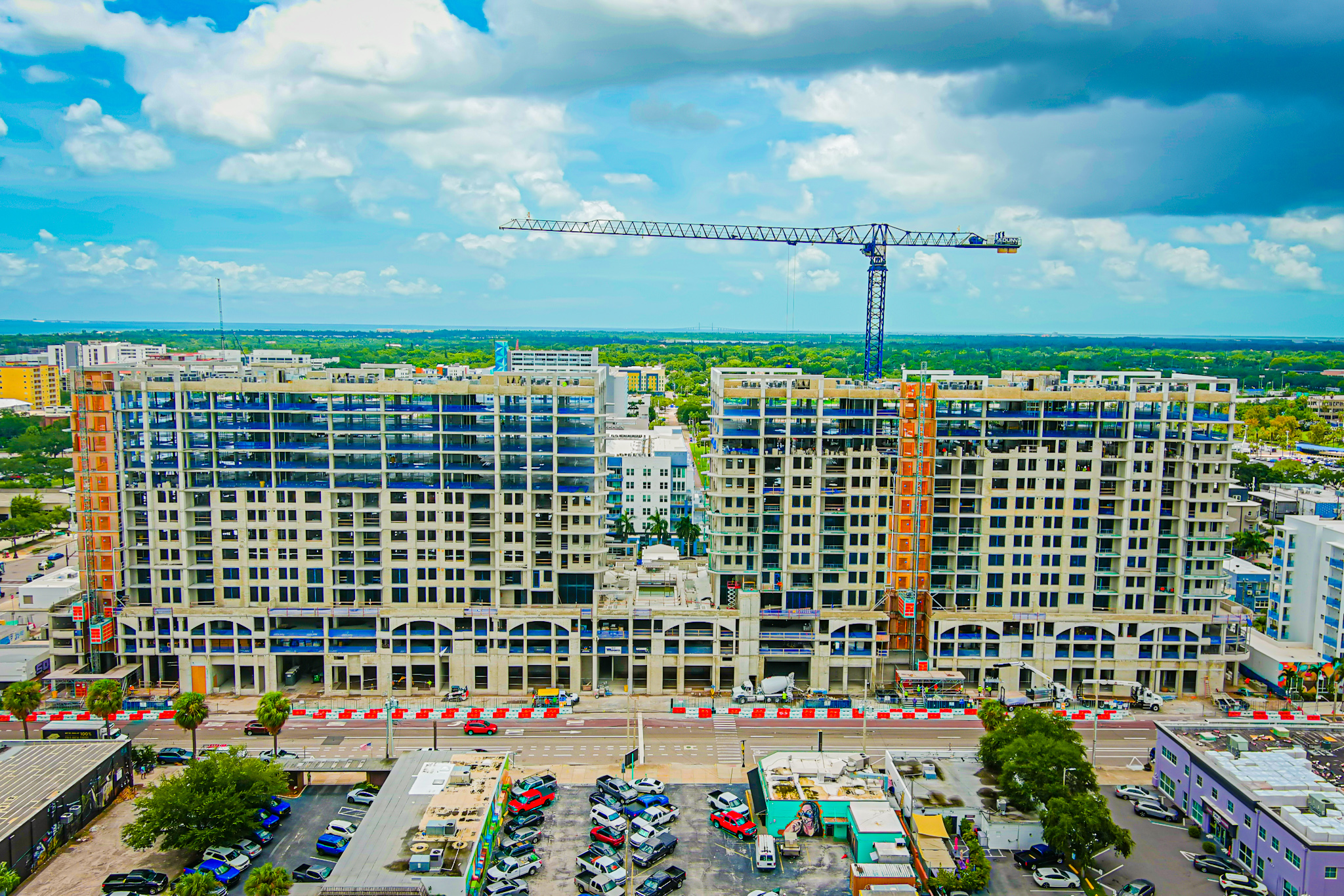 A vibrant aerial photo of a high-rise residential or commercial construction site with a tower crane in the center, taken as part of unmanned aircraft system services to monitor construction progress and site logistics.