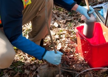 An environmental technician collecting soil samples from a commercial property during a Phase II Environmental Site Assessment, conducted as part of environmental due diligence before property acquisition.